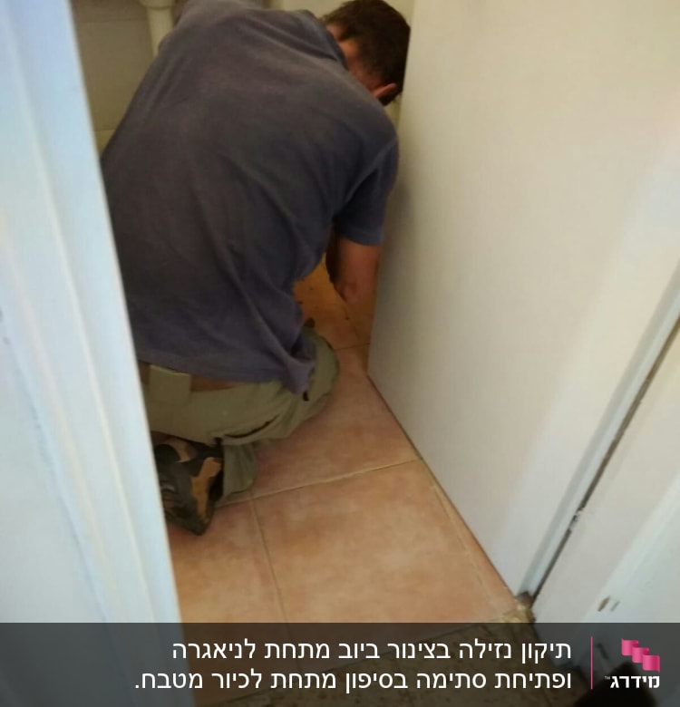 אדם עובד על צנרת מתחת לכיור בחדר אמבטיה
